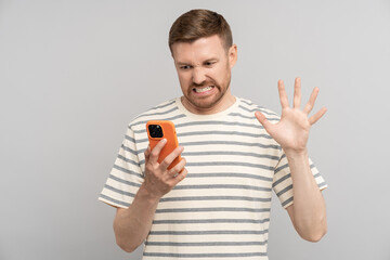 Young man with disgust look at smartphone screen. Portrait of guy cringe and stare with aversion at...