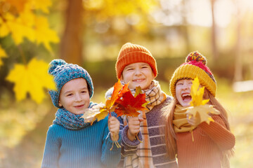 Group of children standing in the autumnal park and holding in their hands bunch of the leaves.