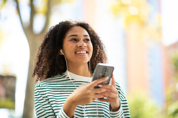 smiling young woman with mobile phone listening with earphones