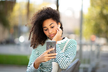 young woman sitting with mobile phone listening with earphones