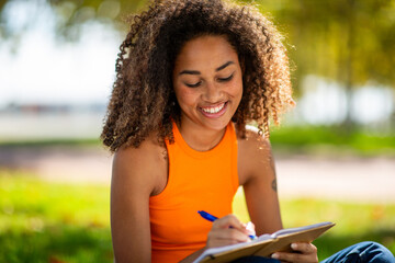 young woman sitting on grass writing in book