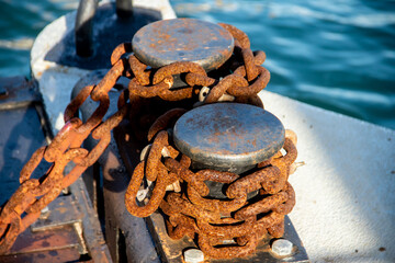 Old abandoned anchor chain with rust and iron cleat,  on a post in a sea dock - obrazy, fototapety, plakaty