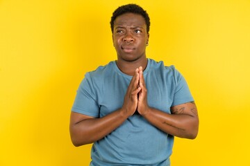 Charming cheerful Young handsome man standing over yellow studio background making up plan in mind holding hands together, setting up an idea.
