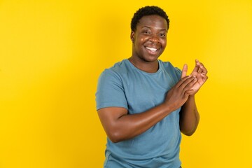 Young handsome man standing over yellow studio background clapping and applauding happy and joyful, smiling proud hands together. - obrazy, fototapety, plakaty