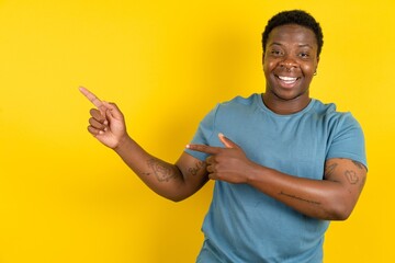 Young handsome man standing over yellow studio background indicating finger empty space showing...