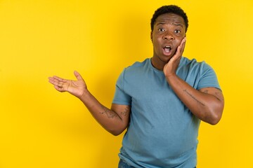 Crazy Young handsome man standing over yellow studio background advising discount prices hold open...