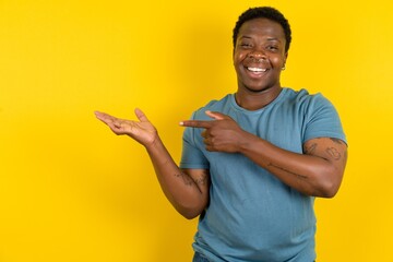 Positive Young handsome man standing over yellow studio background promoter point index finger copyspace hold hand demonstrate offer ads promo - obrazy, fototapety, plakaty