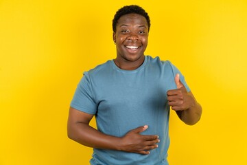 Young handsome man standing over yellow studio background happy positive smile hands on belly show...