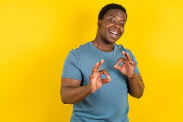 Young handsome man standing over yellow studio background showing both hands with fingers in OK...