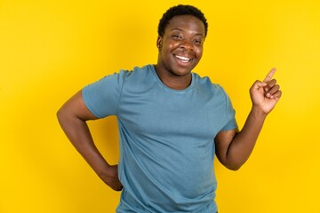 Young handsome man standing over yellow studio background holding finger up having idea and posing