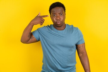 Unhappy Young handsome man standing over yellow studio background makes suicide gesture and...