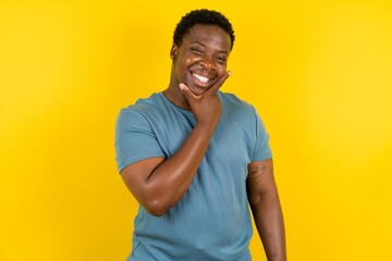Young handsome man standing over yellow studio background looking confident at the camera smiling with crossed arms and hand raised on chin. Thinking positive.