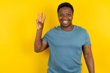 Young handsome man standing over yellow studio background showing and pointing up with fingers number three while smiling confident and happy. - obrazy, fototapety, plakaty