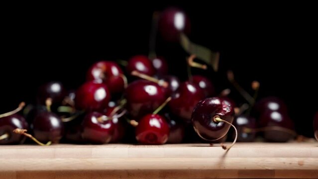 A cherry falls down from a wooden board against a black background, in slow motion.
