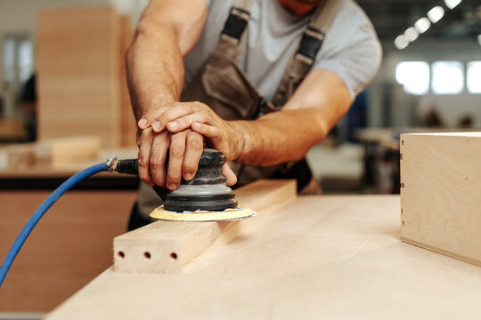 Close up of carpenter hands sanding wood with orbital sander at workshop - Powered by Adobe