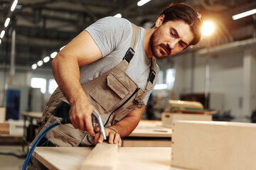 Young carpenter making wood furniture while working in joinery