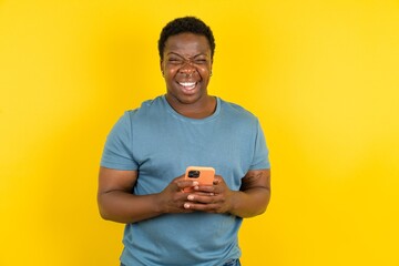 Excited handsome African American standing over yellow studio background  winking and eye hold...
