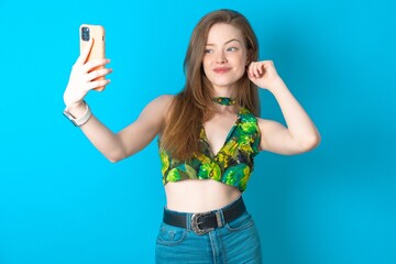 Young beautiful woman wearing top smiling and taking a selfie ready to post it on her social media.