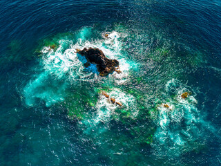 Rochedo maritimo rodeado de água de tonalidades verdes e azuis. 
