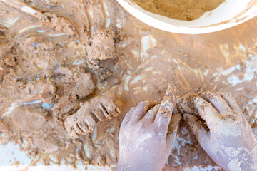 Flat lay of dirty kid hands modelling natural clay out of clay powder