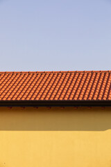 Tetto di tegole rosse sulla parete gialla di una casa nel villaggio. Fotografia verticale.