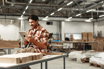 Young carpenter standing in his workshop using a digital tablet