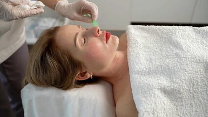 Obraz na płótnie Canvas Professional cosmetic procedures. Young female doctor in a beauty clinic receiving facial microdermabrasion treatment. After the procedure, the master cosmetologist wipes the face from the cream.