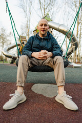 Smiling bald man sitting on a swing in a playground