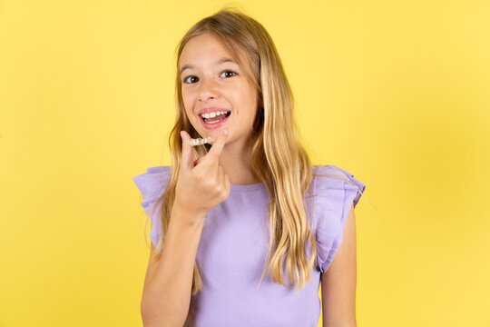 Beautiful caucasian kid girl wearing violet dress holding an invisible aligner ready to use it. Dental healthcare and confidence concept.