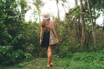 Unrecognizable woman in hat walking in tropical nature