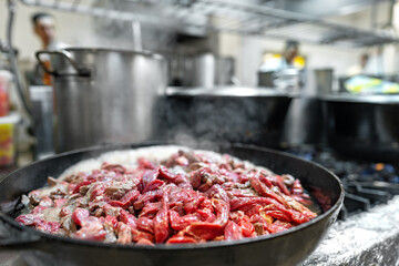 Meat fryed on frying pan on modern stove in professional kitchen