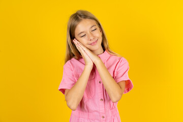 Beautiful caucasian kid girl wearing pink shirt leans on pressed palms closes eyes and has pleasant smile dreams about something