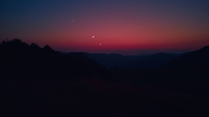Silhouette of a countryside with Milky Way stars, planets and crescent Moon.