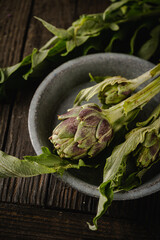 fresh baby artichoke with leaves on rustic wooden background