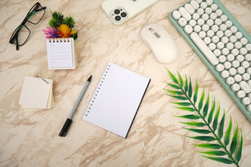 Modern white marble office desk table with keyboard, smartphone and other supplies with stand calendar. Blank notebook page for input the text in the middle. Top view, flat lay.