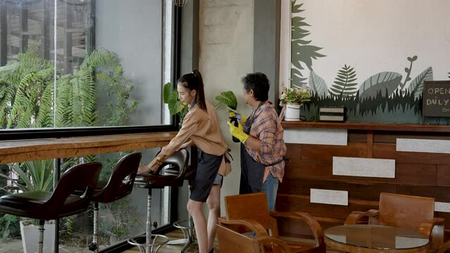 Elderly Asian mothers, with daughter who is owner cafe where two them are helping clean up, two people are helping clean tables, chairs that are soiled with drinks, snacks that customers sit eat.