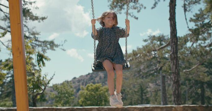 A beautiful smiling happy child is riding on a swing in the forest in the mountains. Fun childhood with laughter in nature. High quality 4k footage