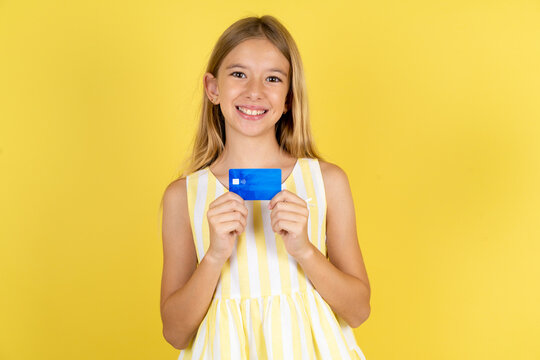Photo of cheerful Beautiful caucasian kid girl wearing yellow dress hold debit card look empty space