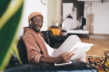 Smiling black man resting on sofa with book in hand
