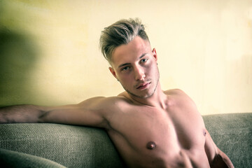 Photo of a handsome blond man with muscular physique lounging on a couch