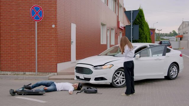 Businesswoman after hitting a person riding an electric scooter with her car. Driver desperately calling for help, ambulance, police, insurance company. The man lies unconscious on the asphalt