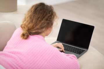Unrecognizable young woman using modern laptop with blank screen at home