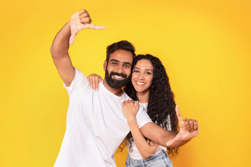 Cheerful Middle Eastern Couple Framing Themselves For Photo, Yellow Background