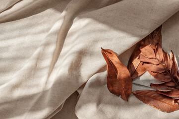 Messy brown fall leaves on neutral beige linen crumpled fabric background with aesthetic natural...
