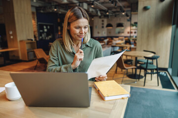Focused woman analyst working with documents and use laptop while sitting in cozy coworking 