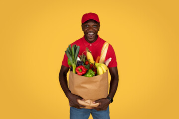 Cheerful shocked millennial african american guy courier hold paper bag with products