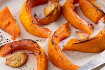 pieces of baked pumpkin with spices and garlic on a beige plate and beige background