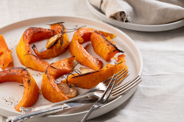 pieces of baked pumpkin with spices and garlic on a beige plate and beige background