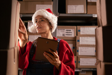 Warehouse female worker uses digital tablet for checking stock in warehouse at Christmas