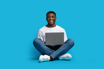 Cheerful millennial black man independent contractor working on laptop